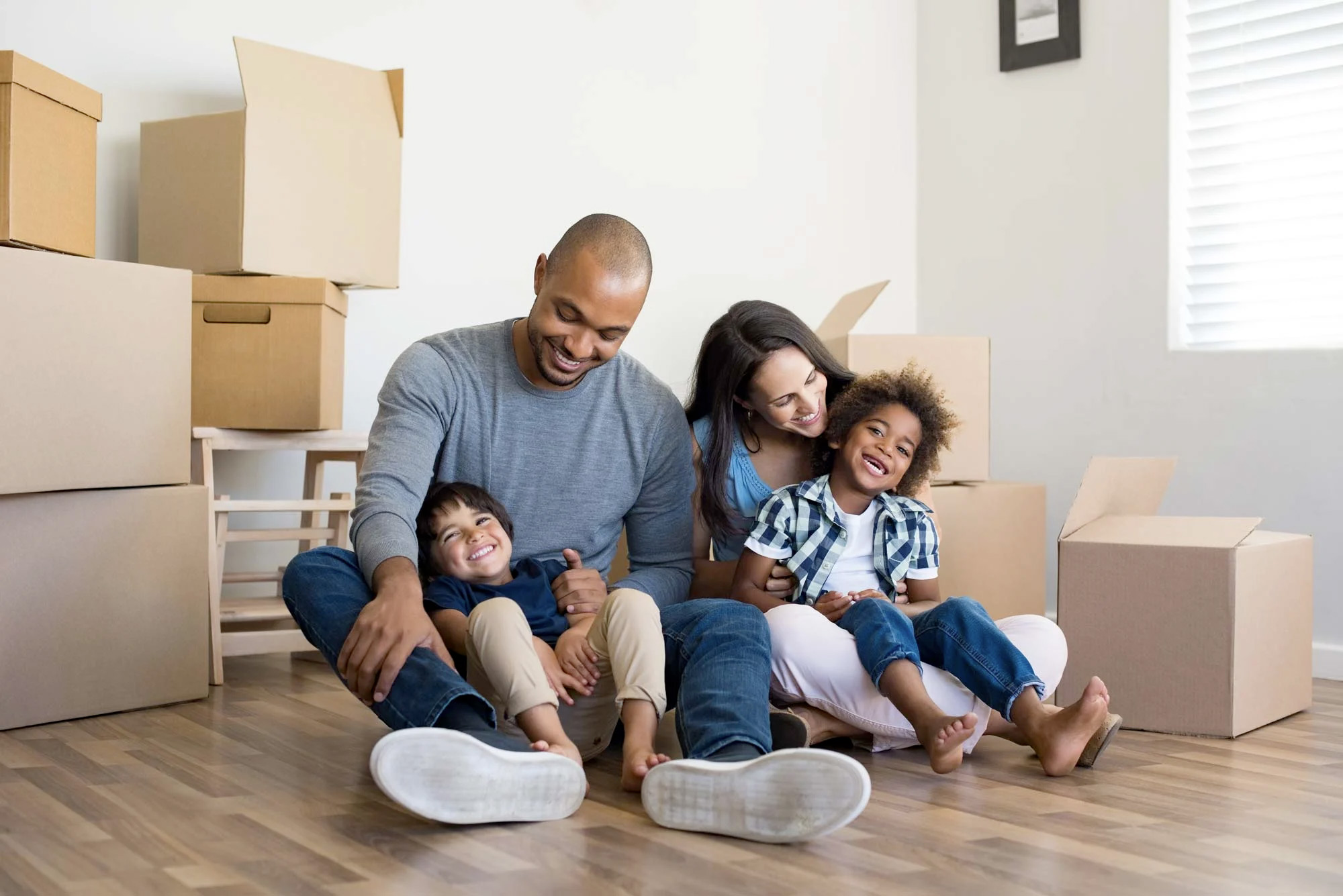 family sitting in living room of recently purchased home with boxes all over the place